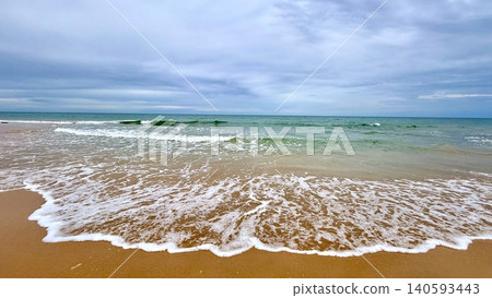 Calm ocean shoreline with gentle waves under cloudy sky Calm ocean shoreline with gentle waves under cloudy sky 140593443