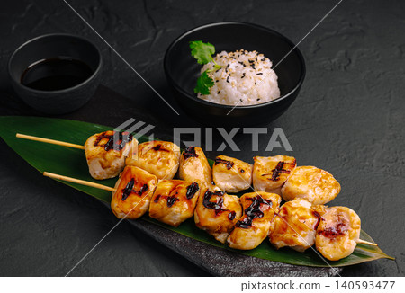 Grilled chicken skewers served with rice and dipping sauce on black surface Grilled chicken skewers served with rice and dipping sauce on black surface 140593477