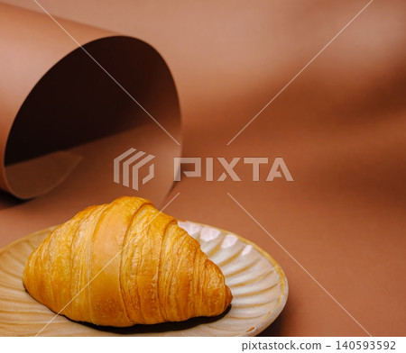 Fresh croissant on a plate with brown background and paper roll 140593592
