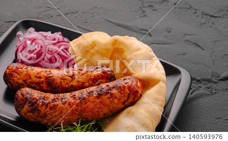 Grilled sausages served with flatbread and onions on a black plate Grilled sausages served with flatbread and onions on a black plate 140593976