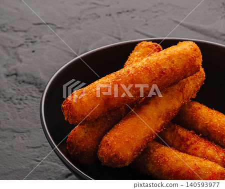 Crispy cheese sticks served in a black bowl on a gray surface 140593977