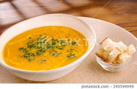 Hot soup with herbs served with bread cubes in a bowl on wooden table 140594049