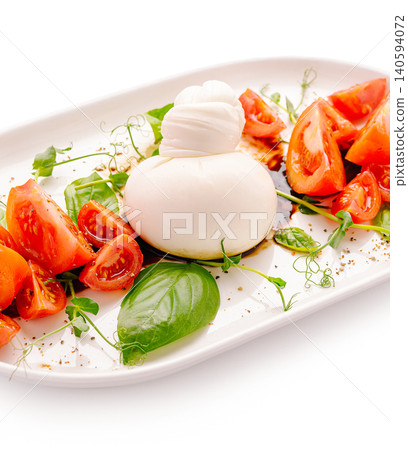 Fresh tomatoes and burrata cheese served on a white plate with greens Fresh tomatoes and burrata cheese served on a white plate with greens 140594072