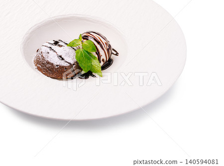 Dessert served on a white plate with chocolate and mint garnish in a restaurant Dessert served on a white plate with chocolate and mint garnish in a restaurant 140594081