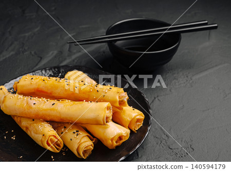 Crispy spring rolls served on a black plate with chopsticks and a bowl Crispy spring rolls served on a black plate with chopsticks and a bowl 140594179
