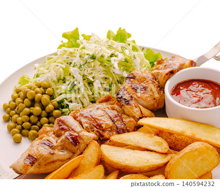Grilled chicken skewer served with potatoes and salad at a dining table 140594232