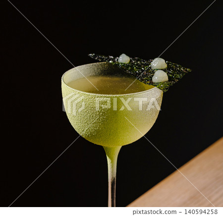 Green cocktail served in a glass on a wooden table against a dark background Green cocktail served in a glass on a wooden table against a dark background 140594258