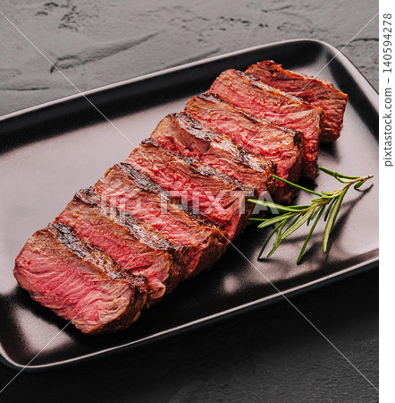 Grilled veal steak served on black plate with fresh rosemary garnish in kitchen 140594278