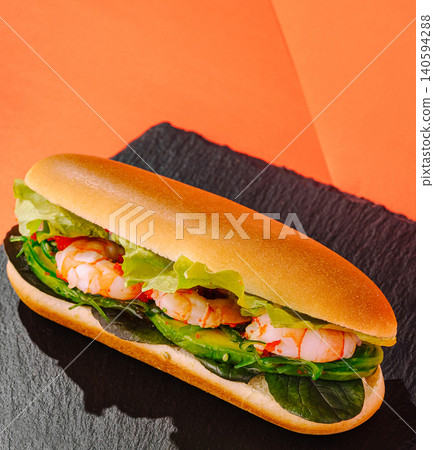 Shrimp sandwich on black plate against bright orange background 140594288