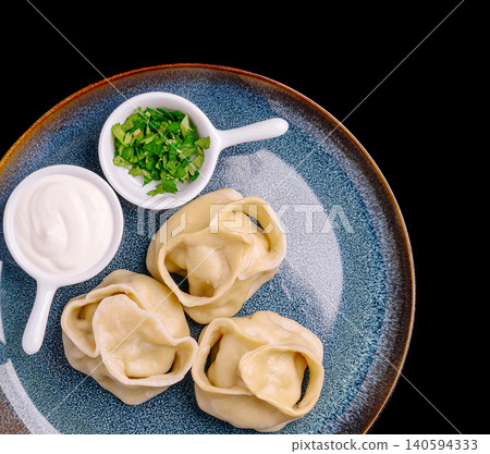 Delicious dumplings served with sour cream and fresh herbs on a dark plate 140594333
