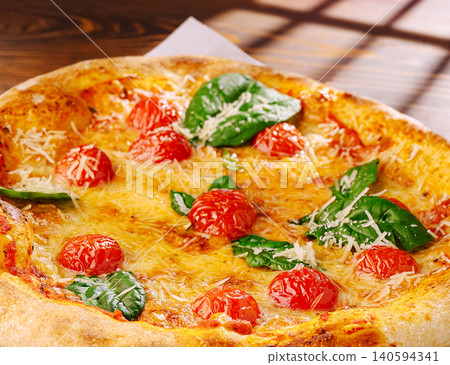 Fresh pizza with tomatoes and spinach on a wooden table in daylight Fresh pizza with tomatoes and spinach on a wooden table in daylight 140594341