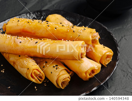 Delicious Spring rolls filled with spiced meat lie on a dark plate Delicious Spring rolls filled with spiced meat lie on a dark plate 140594348