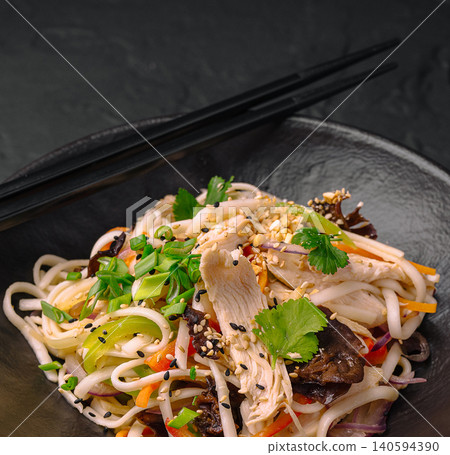 Noodles with vegetables and chicken served in a black bowl with chopsticks Noodles with vegetables and chicken served in a black bowl with chopsticks 140594390