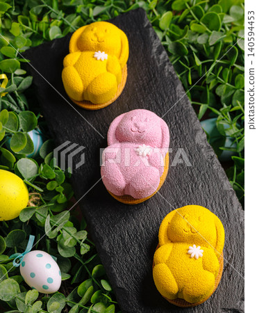 Bunny-shaped desserts on a slate board surrounded by green leaves and eggs 140594453