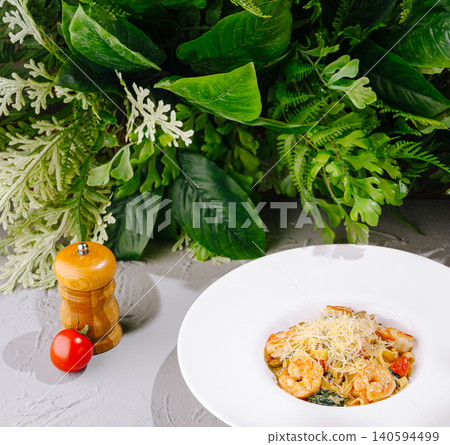 Shrimp pasta served on a white plate with greens in the background Shrimp pasta served on a white plate with greens in the background 140594499