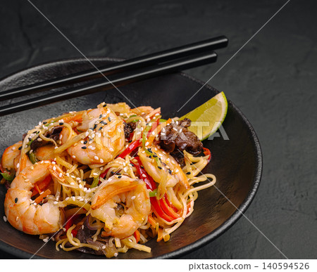 Shrimp stir-fry with noodles and lime served in a black bowl with chopsticks Shrimp stir-fry with noodles and lime served in a black bowl with chopsticks 140594526