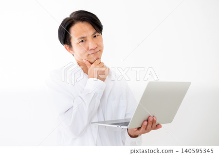 Portrait of a middle-aged man in a white shirt looking thoughtfully at his laptop, against a white background. 140595345
