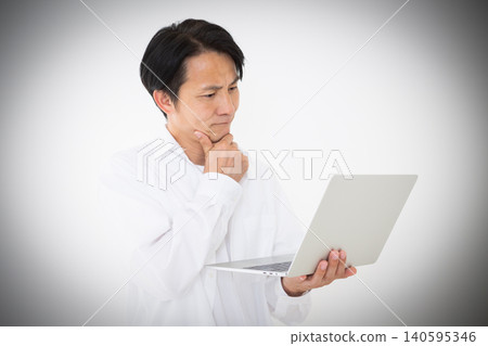 Portrait of a middle-aged man in a white shirt looking thoughtfully at his laptop, against a white background. Portrait of a middle-aged man in a white shirt looking thoughtfully at his laptop, against a white background. 140595346