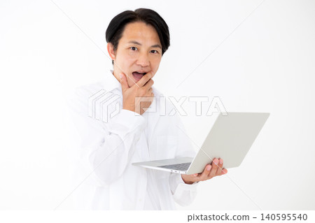 Portrait of a middle-aged man in a white shirt looking surprised at a laptop, against a white background. Portrait of a middle-aged man in a white shirt looking surprised at a laptop, against a white background. 140595540