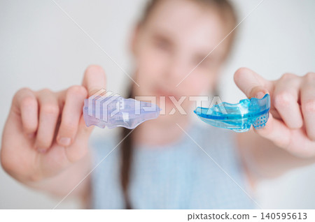 Little girl holding a flexible dental alignment mouthguard for correct bite, pediatric orthodontics routine Little girl holding a flexible dental alignment mouthguard for correct bite, pediatric orthodontics routine 140595613