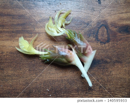 A fresh ginger flower bud with pale yellow blossoms is placed against a wood grain background. A fresh ginger flower bud with pale yellow blossoms is placed against a wood grain background. 140595933