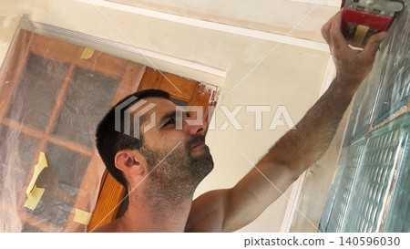 POV of young man uses brush to clean finished wall surface removing dust and small imperfections after renovation work. Male worker carefully prepare smooth wall for next finishing stage inside room POV of young man uses brush to clean finished wall surface removing dust and small imperfections after renovation work. Male worker carefully prepare smooth wall for next finishing stage inside room 140596030