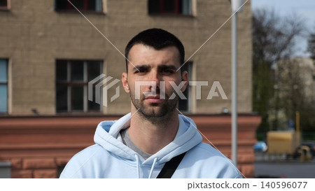 Portrait of young confident bearded man in casual clothing with cityscape background. Close up of handsome guy looks into camera standing at city environment at sunny day Portrait of young confident bearded man in casual clothing with cityscape background. Close up of handsome guy looks into camera standing at city environment at sunny day 140596077
