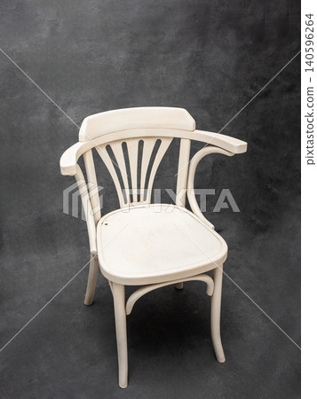 Elegant white wooden chair with curved arms and slatted backrest, set against a textured dark background, showcasing minimalist design and craftsmanship 140596264