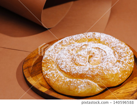 Ensaimada pastry with powdered sugar on wooden plate Ensaimada pastry with powdered sugar on wooden plate 140596588