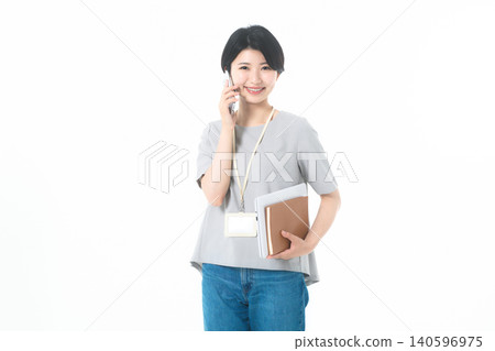 一位年輕女子看著鏡頭,手持文件,在白色背景前打電話。 一位年輕女子看著鏡頭,手持文件,在白色背景前打電話。 140596975