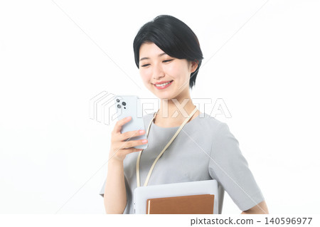 一位年輕女子手持文件,在白色背景下查看智慧型手機,臉上帶著微笑。 一位年輕女子手持文件,在白色背景下查看智慧型手機,臉上帶著微笑。 140596977