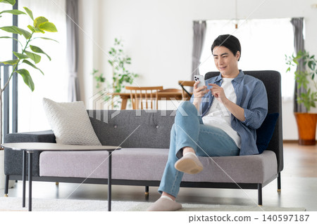 A middle-aged man sitting on the living room sofa, looking at his smartphone. 140597187