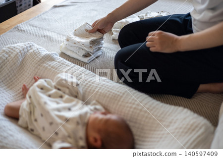 A mother folds laundry next to her sleeping newborn. A mother folds laundry next to her sleeping newborn. 140597409