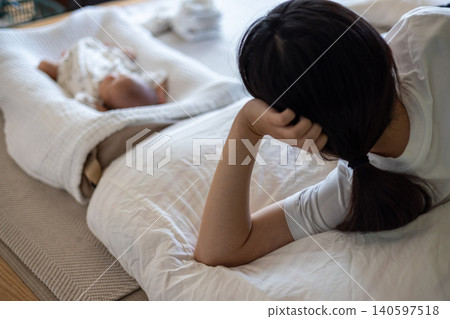 A mother, exhausted from childcare, is sleeping on the futon next to her newborn, using her elbow as a pillow. A mother, exhausted from childcare, is sleeping on the futon next to her newborn, using her elbow as a pillow. 140597518