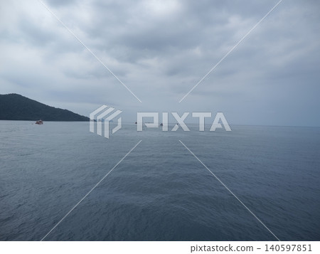 Calm sea under cloudy sky with distant boat and forested coast 140597851