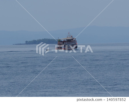 Passenger ferry boat on calm blue sea near distant island, misty horizon Passenger ferry boat on calm blue sea near distant island, misty horizon 140597852