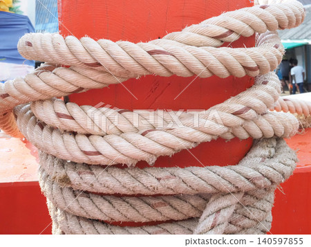 Mooring rope wrapped around red bollard at harbor dock with worn fiber texture Mooring rope wrapped around red bollard at harbor dock with worn fiber texture 140597855