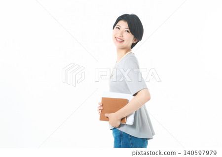 A young woman with a smile, holding documents and looking back, against a white background. A young woman with a smile, holding documents and looking back, against a white background. 140597979