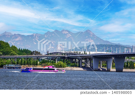 Pink cruise ship on a wide river under beautiful blue sky with majestic mountains Pink cruise ship on a wide river under beautiful blue sky with majestic mountains 140598003