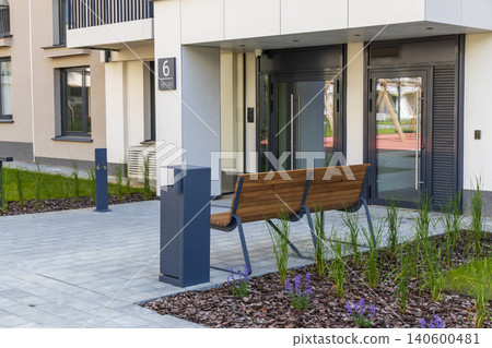 Paved courtyard with a minimalist bench and trash bin outside a new housing block 140600481