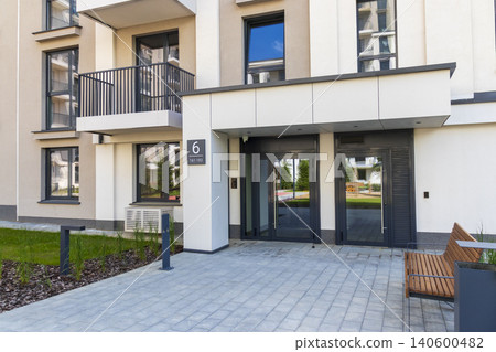 Paved courtyard with a minimalist bench and trash bin outside a new housing block 140600482