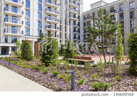 Modern residential courtyard with green landscaping, pine trees, and a kids playground 140600566