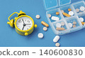 Pills and vitamins with pill organizer box and alarm clock on a blue background, daily medication and supplement concept 140600830
