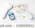 Daily pill box with capsules and medication, digital thermometer and pulse oximeter, and alarm clock on white background 140600832