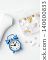Pill organizer, digital thermometer, and alarm clock on white background, daily medication and supplement 140600833