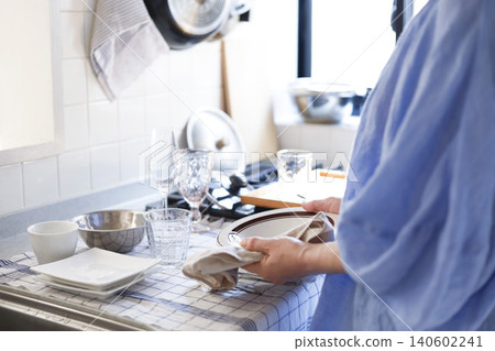 A woman drying dishes in a brightly lit kitchen. A woman drying dishes in a brightly lit kitchen. 140602241