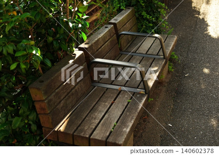 A wooden bench in a quiet park, bathed in dappled sunlight; a moment of everyday rest and a nostalgic scene. A wooden bench in a quiet park, bathed in dappled sunlight; a moment of everyday rest and a nostalgic scene. 140602378