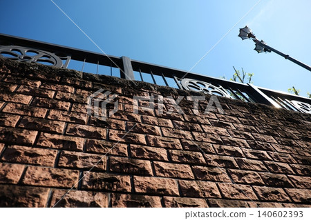 A low-angle view looking up at the brick wall stretching towards the blue sky and the retro streetlights. A low-angle view looking up at the brick wall stretching towards the blue sky and the retro streetlights. 140602393