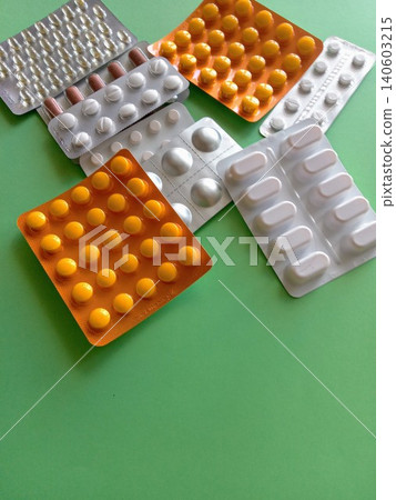 A bunch of pills are scattered on a green surface The pills are of different colors and shapes, and they appear to be in various stages of being opened. Concept of disarray and confusion 140603215