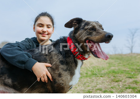 Happy Girl with dark hair in blue hoodie hugs her dog outdoors Happy Girl with dark hair in blue hoodie hugs her dog outdoors 140603304